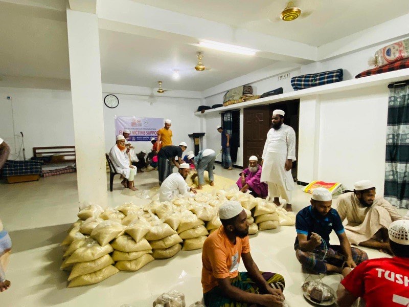Volunteers packing rice into family-sized bags beneath a Flood Victims Support banner